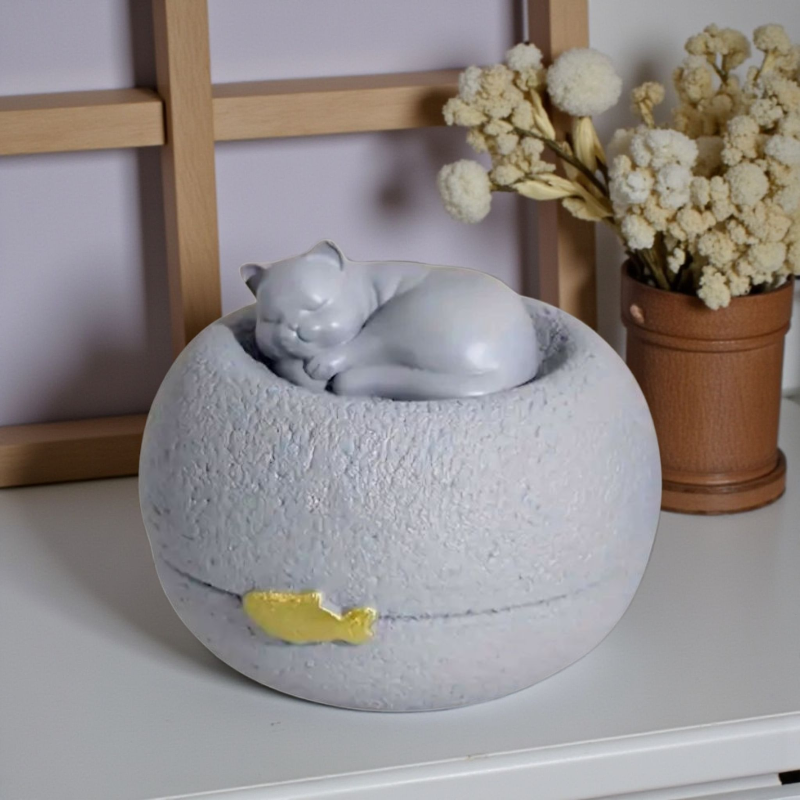 Grijze kattenurn: een vredig slapend poesje bovenop een ronde, steenachtige basis, met een subtiel gouden visje als detail