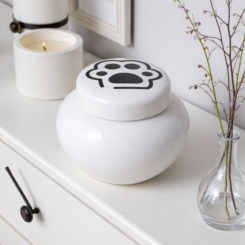 Witte keramische kattenurn met zwarte pootafdruk op het deksel