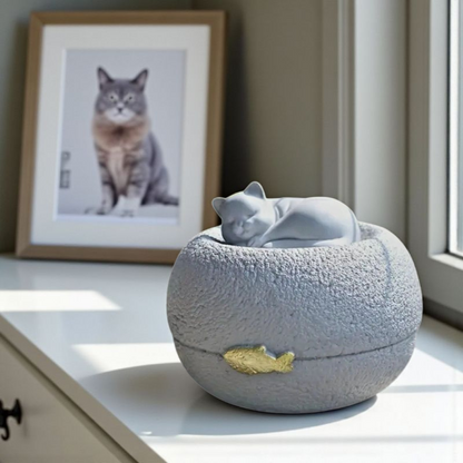 Grijze kattenurn: een vredig slapend poesje bovenop een ronde, steenachtige basis, met een subtiel gouden visje als detail