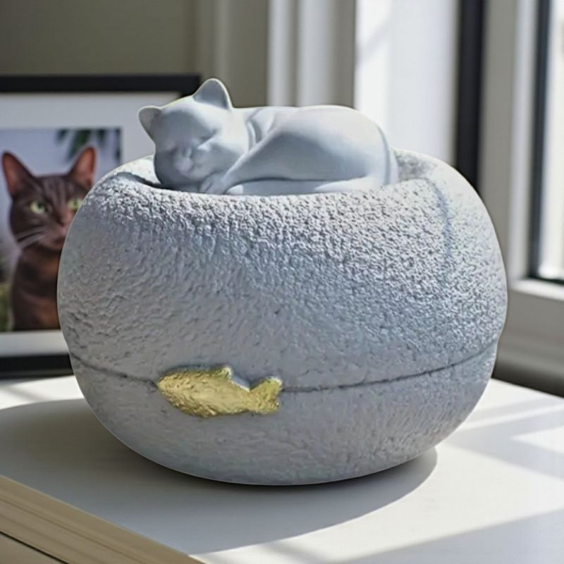 Grijze kattenurn: een vredig slapend poesje bovenop een ronde, steenachtige basis, met een subtiel gouden visje als detail