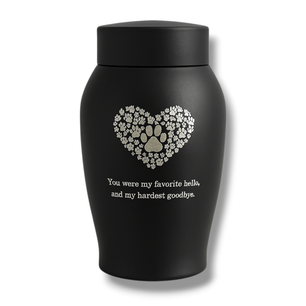 Zwarte matte urn met hart van pootafdrukken en troostende tekst, gefotografeerd tegen een lichte achtergrond.

